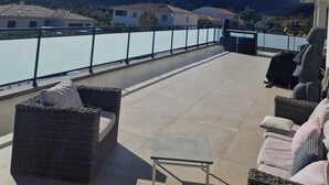 A terrace with wicker furniture, a small table, and a view of a lake and mountains. - Villa Moderne 5 Min Mer - Piscine Idéale Familles, Proche Station de Ski 🏖️❄️ (Ventiseri)