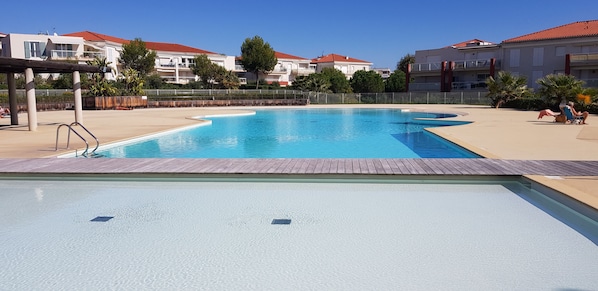 A swimming pool with a wooden deck, surrounded by buildings with red roofs. - Large 3P apartment in estate on top floor with waterfront sea view (Antibes)