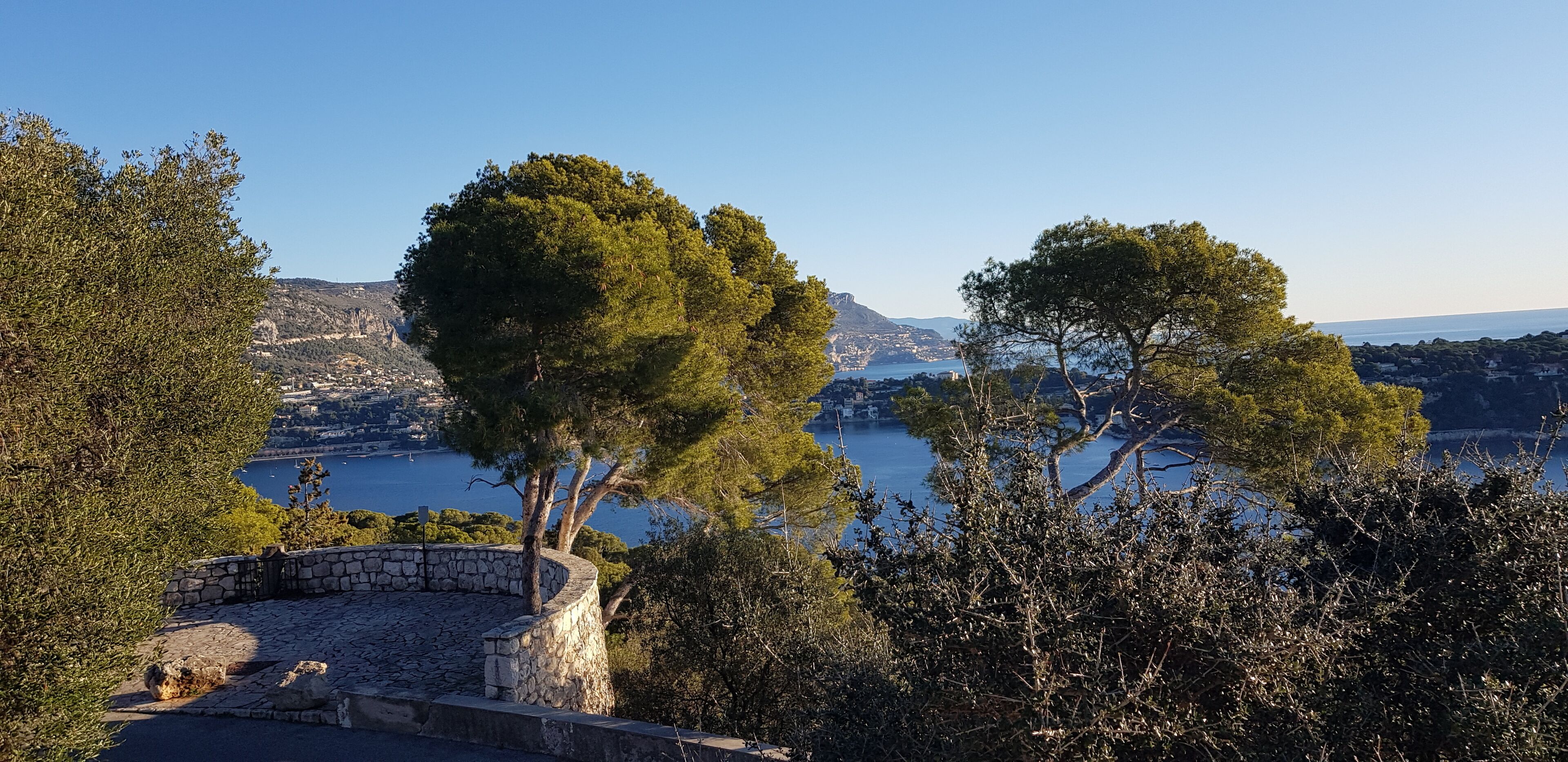 Un sentiero in pietra conduce a un punto panoramico con vista su un lago e colline lontane.