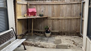 Un jardin avec une clôture en bois, un barbecue, un banc et un pot de fleurs.