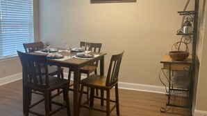 Un coin repas avec une table en bois dressée pour quatre personnes, entourée de chaises. Un tableau est accroché au mur, au-dessus de la table.