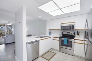 A modern kitchen with white cabinets, stainless steel appliances, and a skylight.