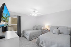 A hotel room with two beds, a TV, a ceiling fan, and a window with blinds.