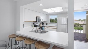 Una cucina moderna con mobili bianchi, un lavello in acciaio inossidabile e un angolo bar con sgabelli.