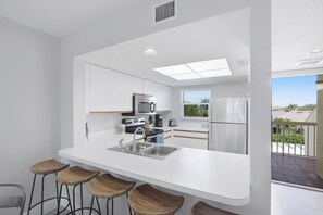 Cozinha moderna com armários brancos, uma pia de aço inoxidável e um balcão com banquetas.