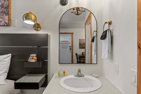 Un baño moderno con un espejo grande, un lavabo, un perchero y una mesita de noche con un tarro.