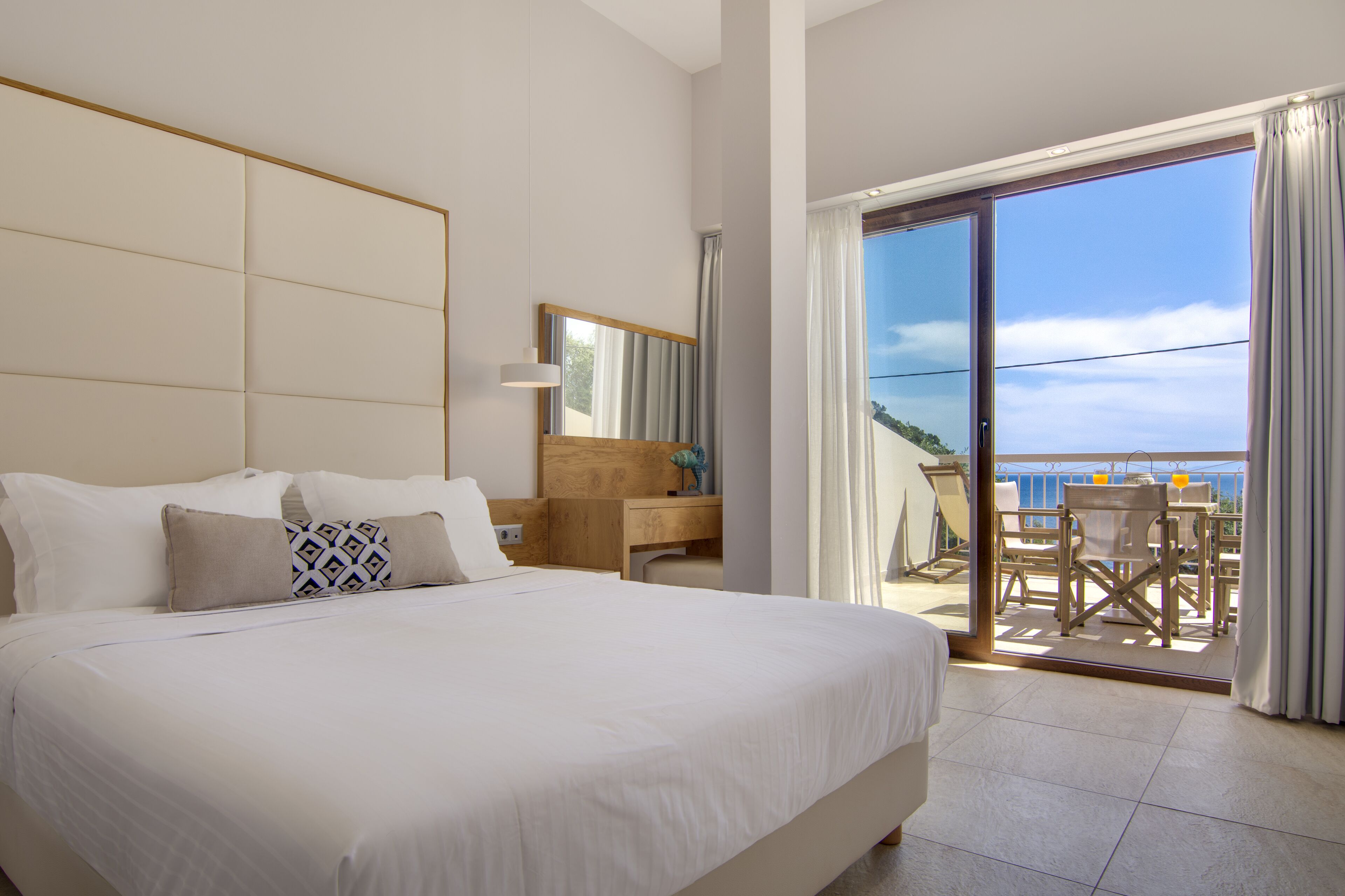 Een hotelkamer met een groot bed, een houten bureau, een stoel en een balkon met uitzicht.