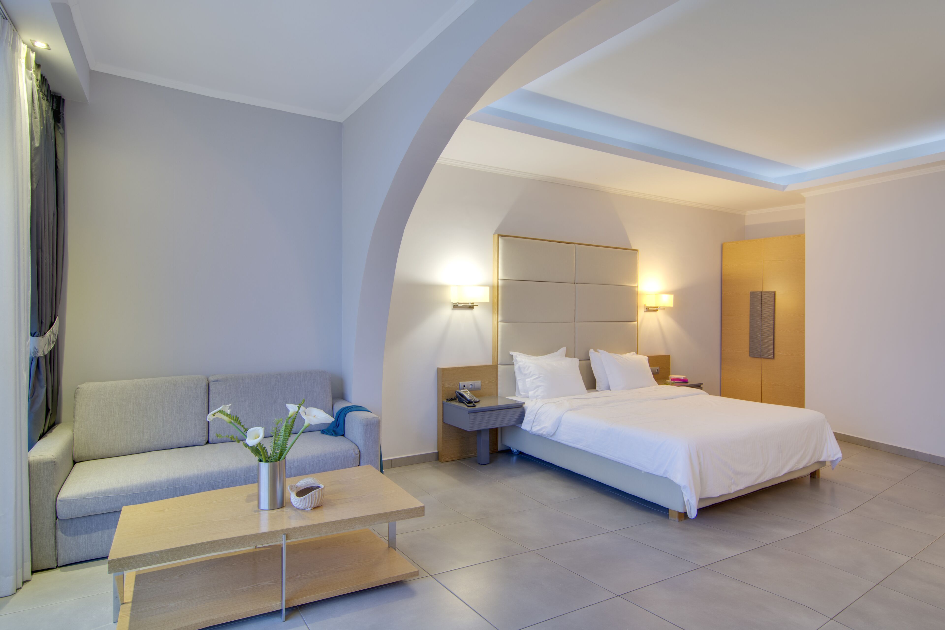 A modern hotel room with a bed, a sofa, a coffee table, and a nightstand.