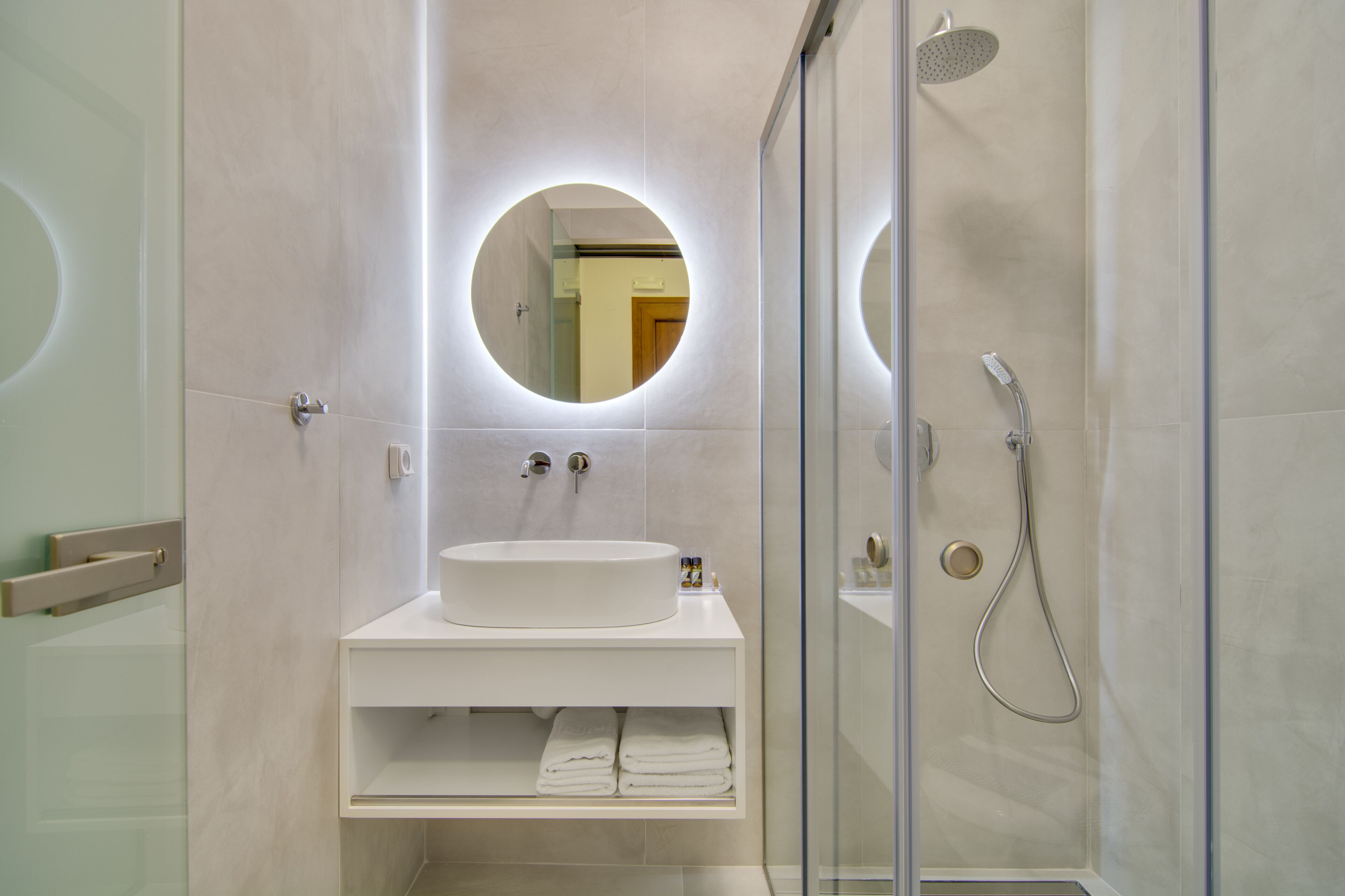 A modern bathroom with a round mirror, a sink, and a shower.