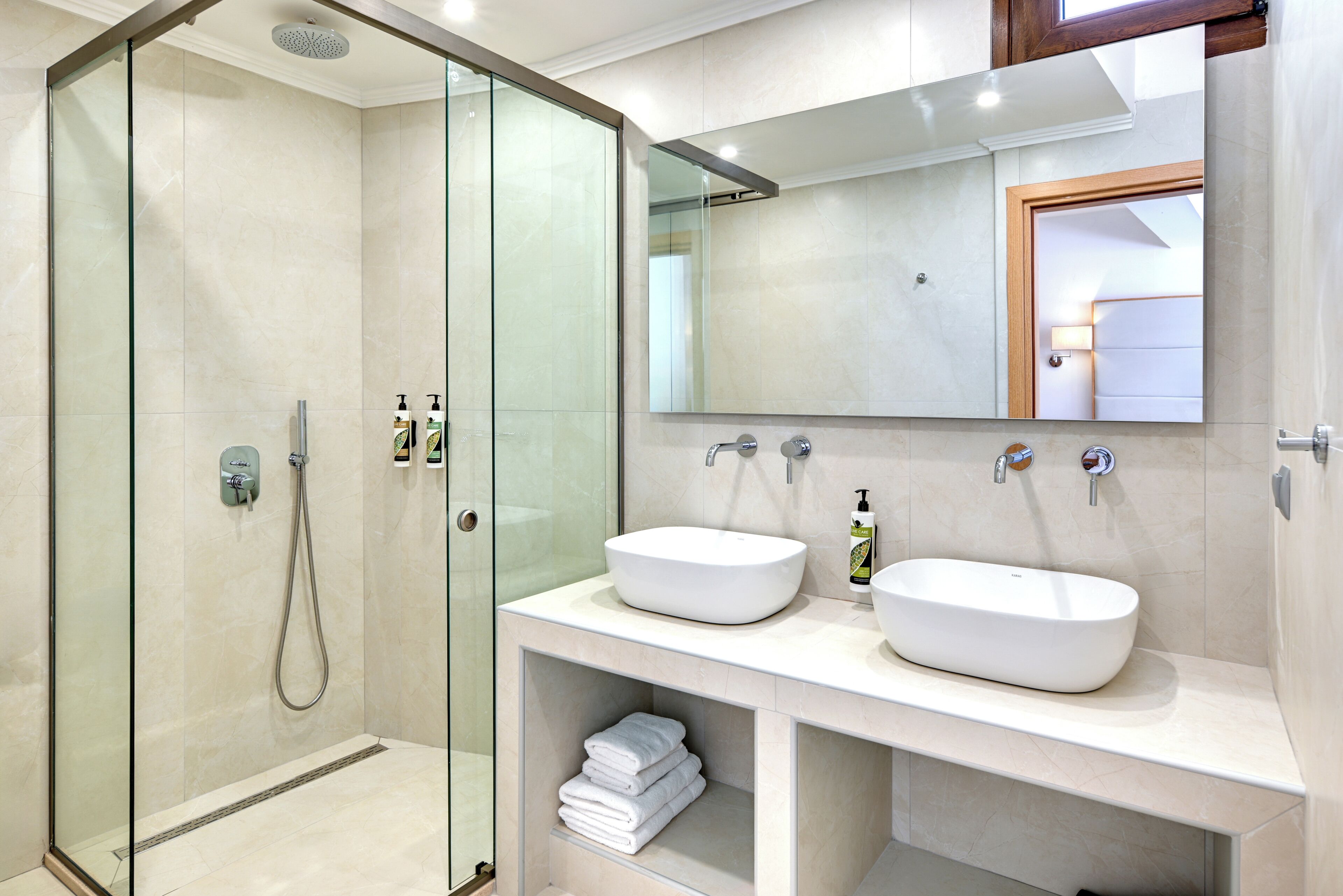 Une salle de bain moderne avec une douche à parois de verre, deux lavabos et un grand miroir.