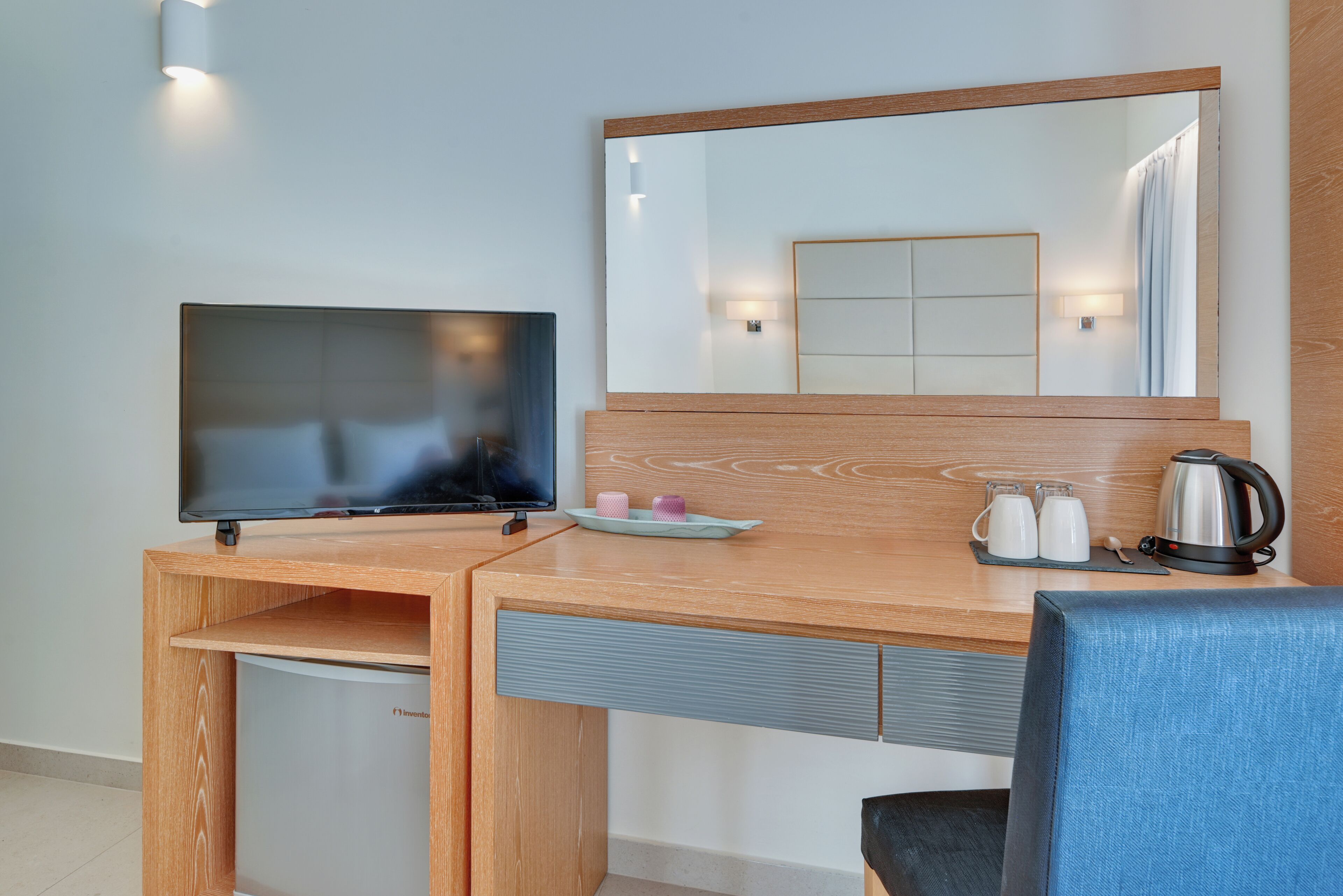 Quarto de hotel com escrivaninha de madeira, televisão, espelho e cafeteira.