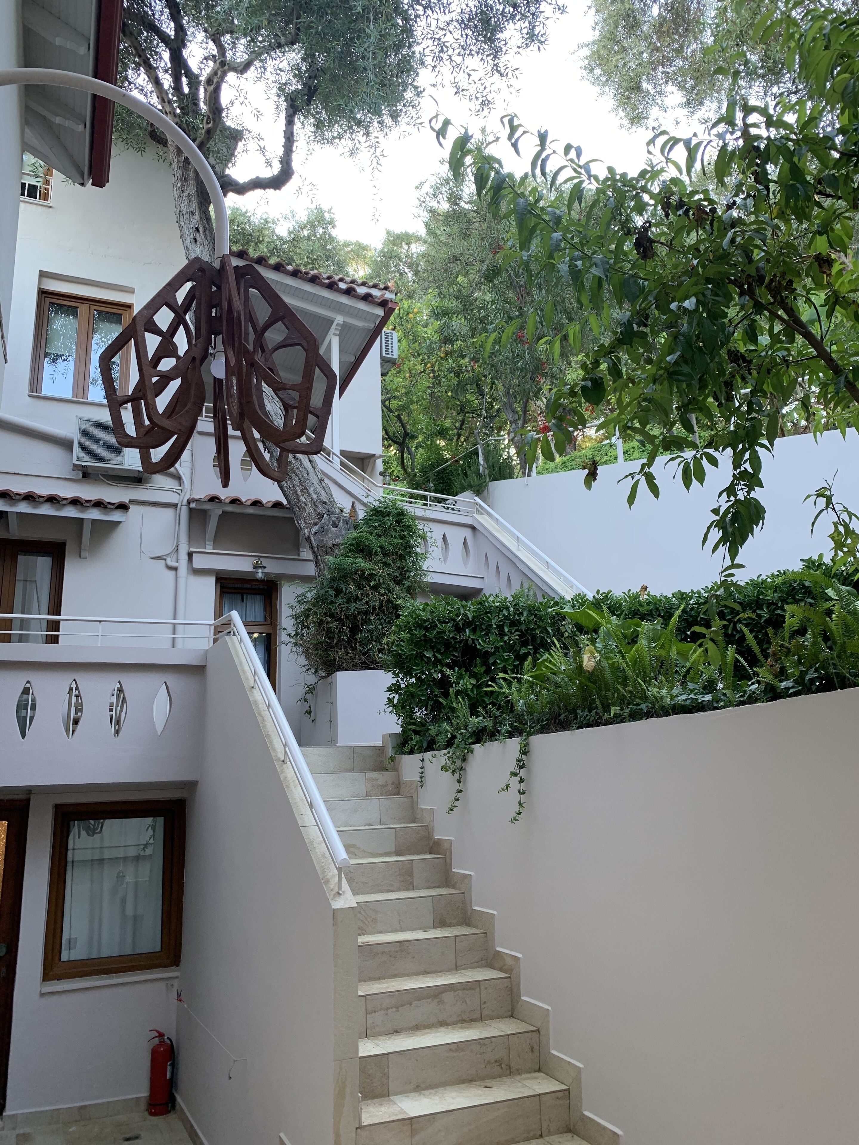 A staircase leading up to a building with a decorative metal sculpture, surrounded by greenery and trees.