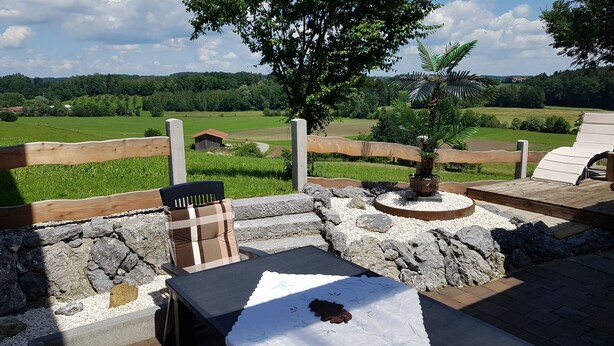 Un banc en pierre avec une table, une clôture en bois et une vue sur des champs verdoyants et un arbre.