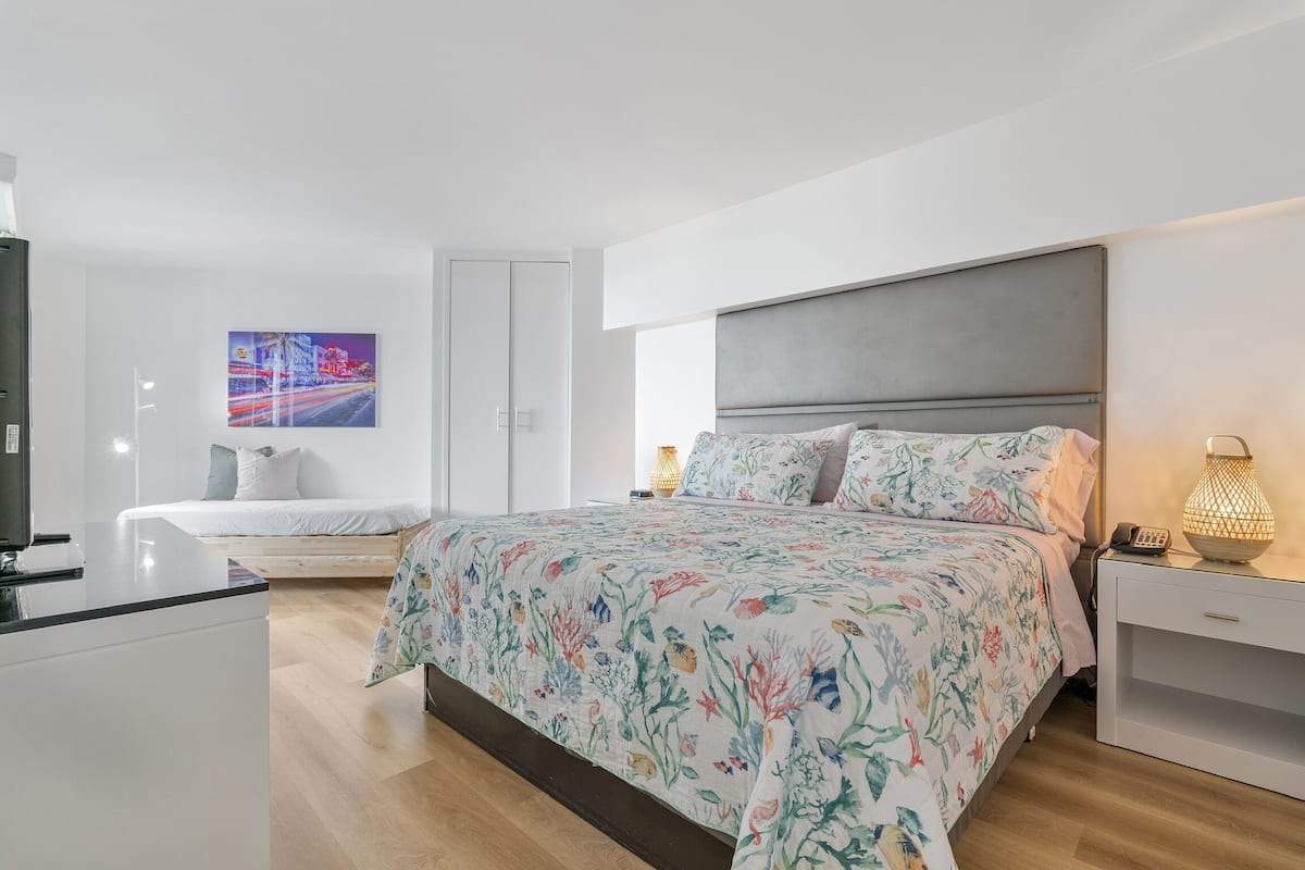 A modern bedroom with a large bed, bedside tables, a TV, and a painting on the wall.