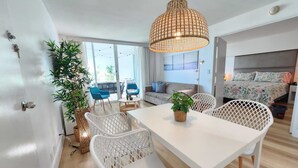 Ein modernes Wohnzimmer mit einem weißen Esstisch, Korbstühlen und einer Pendelleuchte.