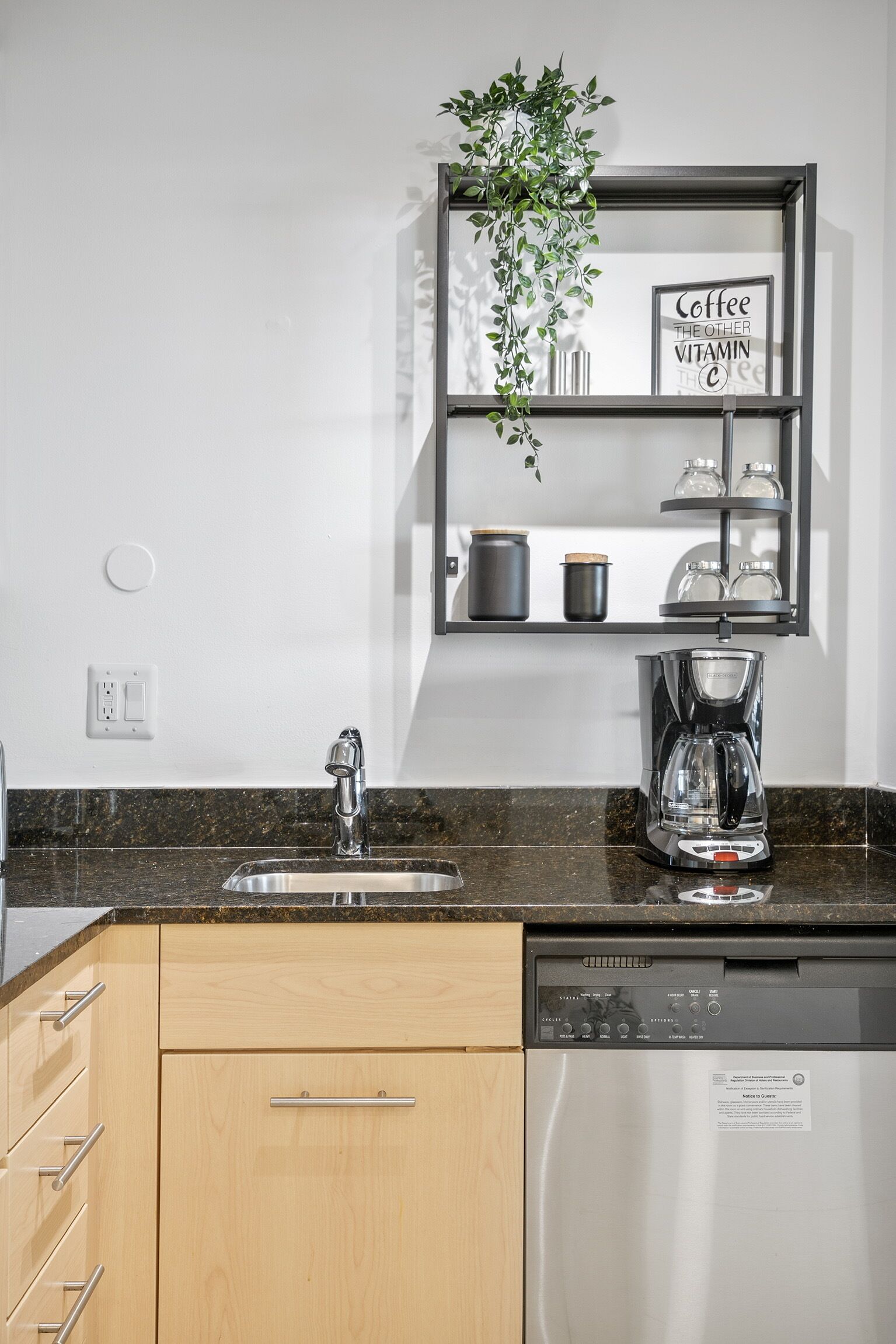 A modern kitchen with a built-in dishwasher, a coffee maker, and a shelf with kitchenware.