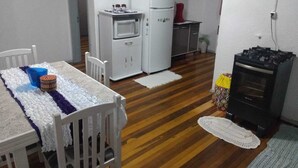 A compact kitchen with a white refrigerator, microwave, and stove, a dining table with chairs, and a small cabinet.