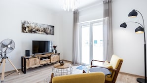 A modern living room with a wooden floor, a TV, a fan, and a sofa.