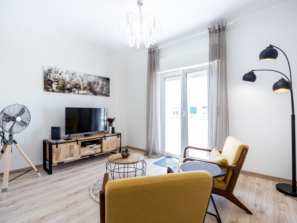 Una sala de estar moderna con piso de madera, televisor, ventilador y sofá.
