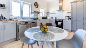 A modern kitchen with white cabinets, a round dining table with a fruit centerpiece, and a pendant light above.