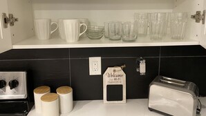 Eine Küche mit weißen Regalen, die weiße Tassen und klare Gläser, einen Toaster und ein Holzschild mit einem WLAN-Passwort beherbergen.