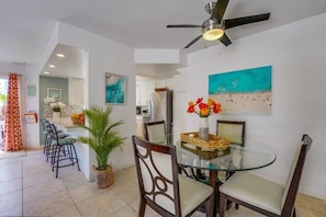 A modern dining area with a glass table, dark wooden chairs, and a ceiling fan.