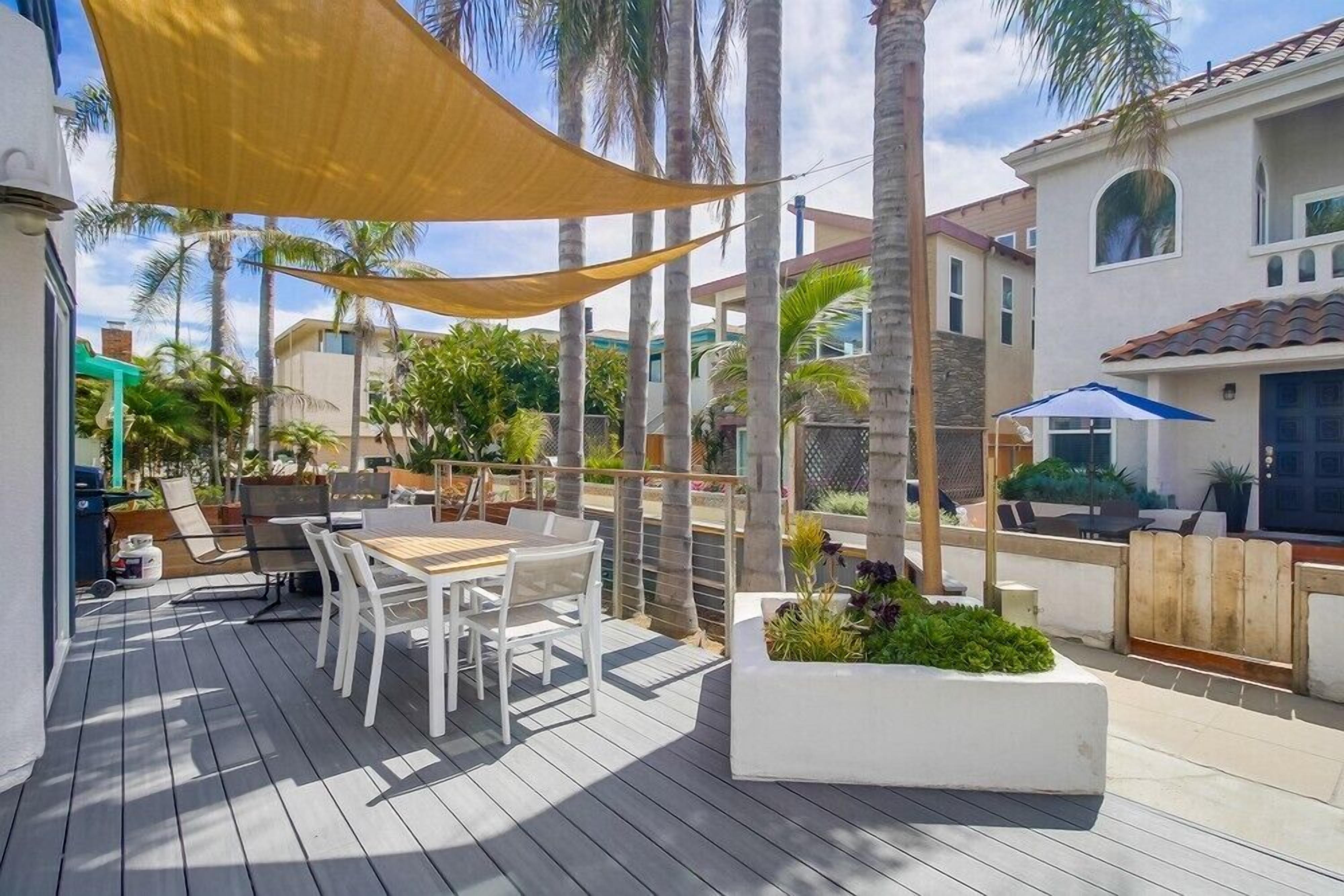 An outdoor patio with a wooden deck, white furniture, and a yellow shade sail.