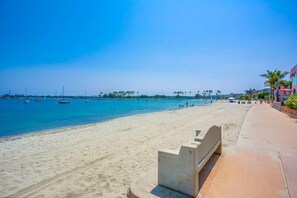 A beach with a sandy shore, a clear blue sea, and a few boats in the distance.