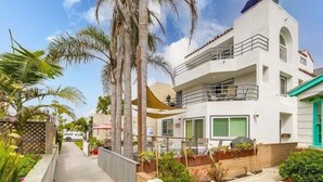Una moderna casa a due piani con un balcone, immersa nel verde e circondata da palme.