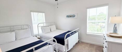 A bedroom with two beds, a ceiling fan, a bedside table with a lamp, and a window with blinds.