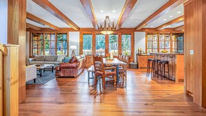 A spacious living area with a wooden ceiling, large windows, a dining table, and a kitchen area with bar stools. - Alpine Star | Stay on the Green @ Family Friendly Rates (Cle Elum)