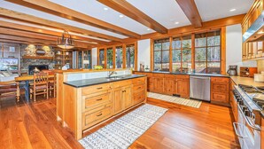 A spacious kitchen with wooden cabinetry, a large island, and a stone fireplace. - Alpine Star | Stay on the Green @ Family Friendly Rates (Cle Elum)