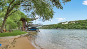 A lakeside property with a wooden deck, a pool, and a view of the lake and hills. - Above Lakeside I Lakefront | Pickleball I Pool/Spa l Firepit I Luxe Services (Austin)