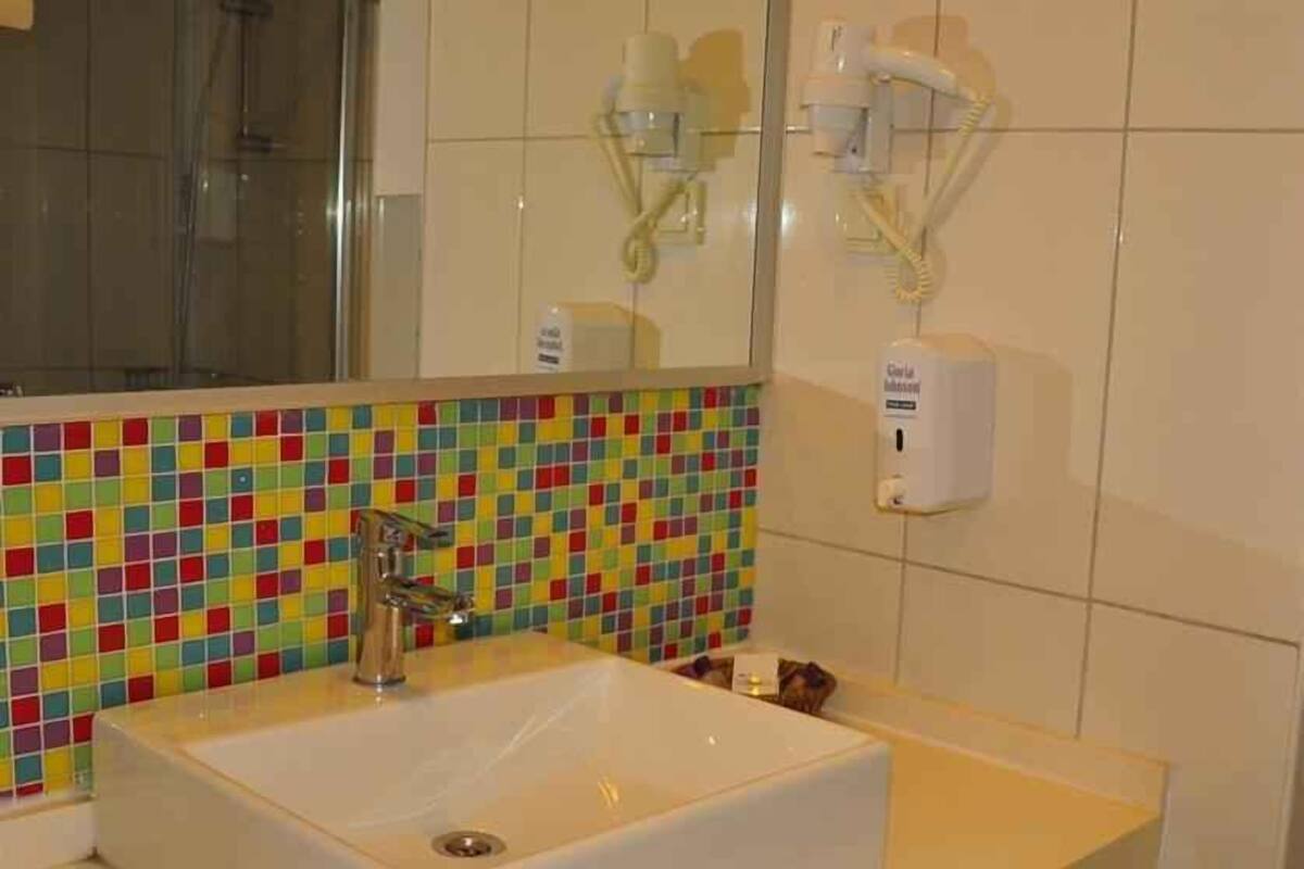 Un baño con un colorido revoque de mosaicos, un lavamanos blanco, un espejo y un secador de manos.