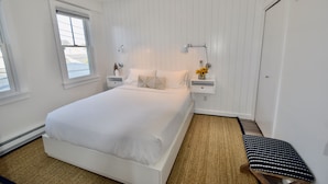 Une chambre à coucher avec un grand lit, deux tables de chevet, une commode, une lampe, un banc et une fenêtre.