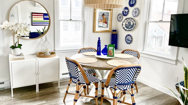 Un coin repas comprenant une table ronde, quatre chaises, un miroir et un mur décoré d’assiettes bleues et blanches.