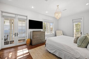 A bedroom with a large bed, a TV mounted on the wall, and a chandelier. - Rosemary Home with Private Pool and Bikes (Rosemary Beach)