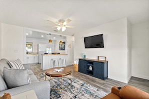 A living room with a sofa, a coffee table, a TV mounted on the wall, and a kitchen area in the background. - Paradise Palms - Nautilus Suite - Heated Pool! (St. Augustine)