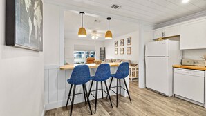 A modern kitchen with white cabinetry, a built-in oven, and a dishwasher. There are three blue bar stools and pendant lights above the counter. - Paradise Palms - Nautilus Suite - Heated Pool! (St. Augustine)