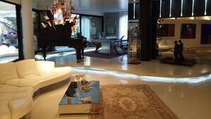 A spacious living room with a grand piano, a white sofa, a glass coffee table, and a modern chandelier. - Luxury Design Apartment | Total Sea View & Private Jacuzzi (La spezia)