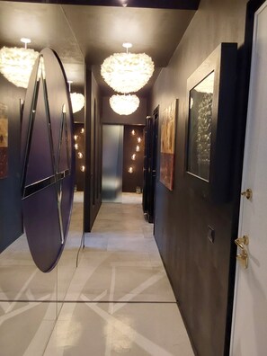 Un couloir au décor moderne, avec notamment un luminaire original au plafond et des œuvres d’art encadrées accrochées aux murs.