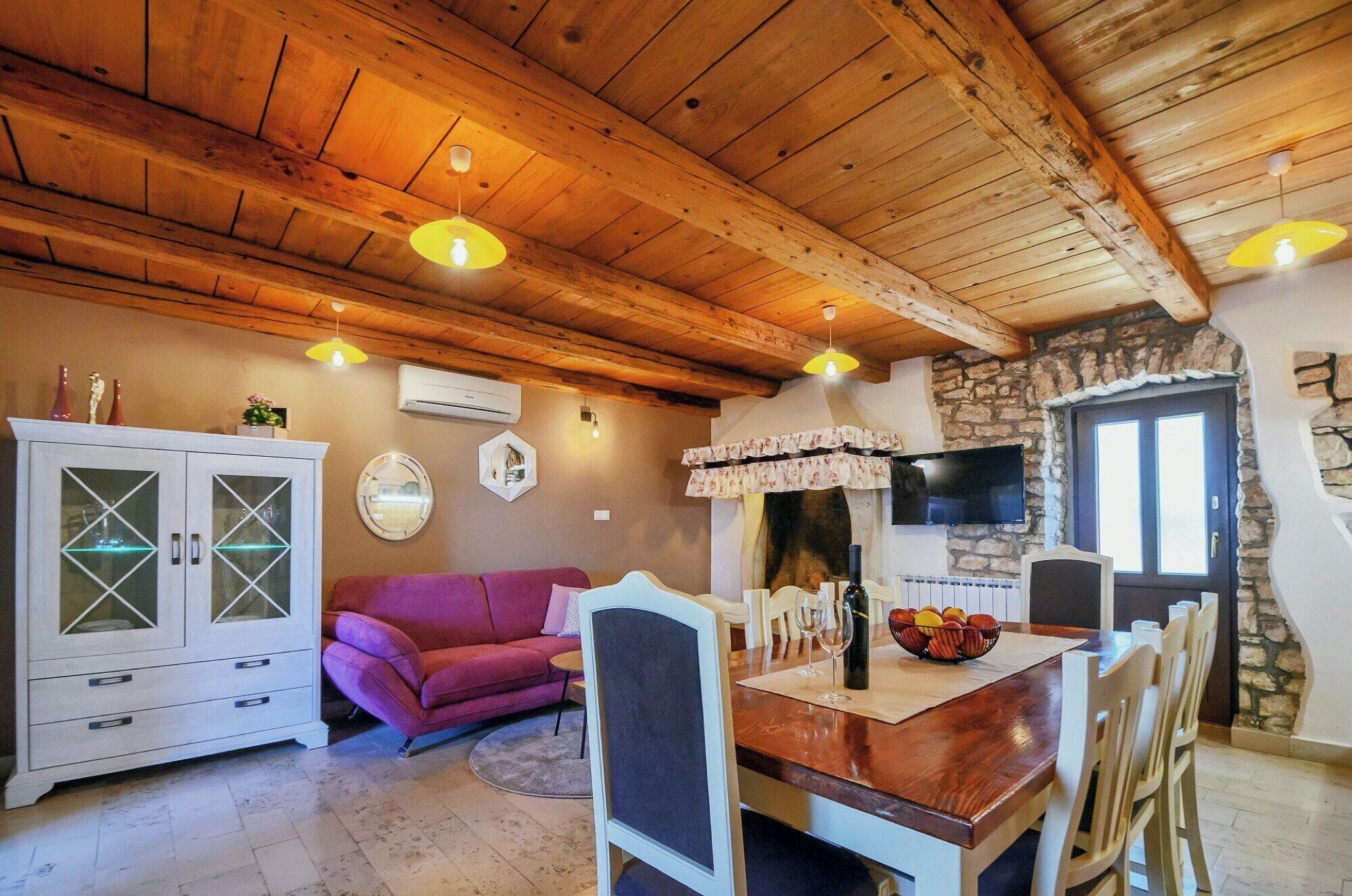 Un soggiorno accogliente con soffitto in legno, un divano viola, un tavolo da pranzo con sedie e un camino in pietra.