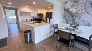 A modern kitchen with white cabinetry, a central island, and a dining area with a table set for four.