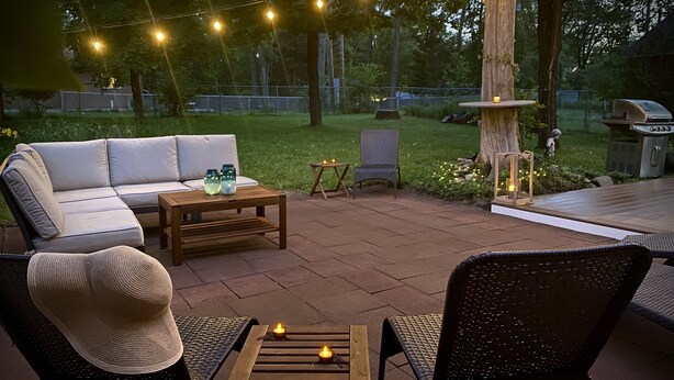 Eine Terrassenanlage im Freien mit einer Couch, zwei Sesseln, einem kleinen Tisch und Lichterketten.