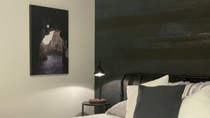 Ein Schlafzimmer mit Bett, Kissen, Nachttisch, Lampe und einem gerahmten Bild an der Wand.