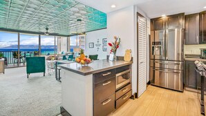 A modern kitchen with a large island, stainless steel appliances, and a view of the ocean. - Hawaii Life Rentals - Kahana Ocean Front (Lahaina)