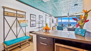 A modern kitchen with a large island, a bench, and a view of the mountains. - Hawaii Life Rentals - Kahana Ocean Front (Lahaina)