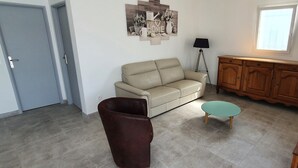 Ett vardagsrum med en beige soffa, en brun fåtölj, ett litet turkost bord, ett träskåp och en golvlampa.