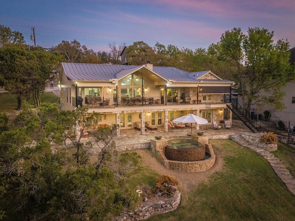 A two-story house with a large patio, outdoor seating, and a stone fire pit.