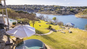 Un espace piscine doté d’un jacuzzi, d’un parasol et offrant une vue sur un lac, avec des maisons en arrière-plan.